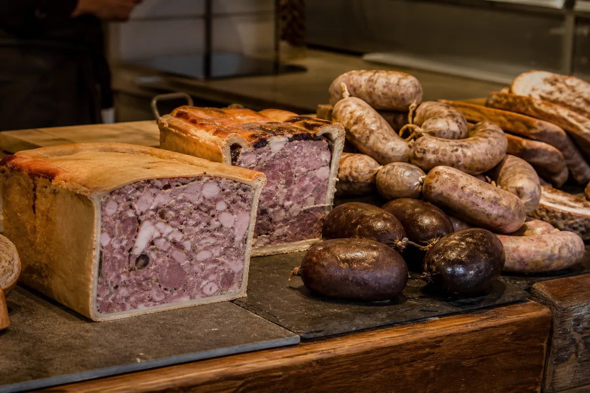 Etal de charcuterie avec terrines entamees, boudins et saucisses en boyau naturel